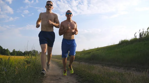 Zwei muskulöse Männer, die im Freien rennen. Junge athletische Jungs joggen über das Feld. männliche Sportler, die gemeinsam in der Natur trainieren. Freunde, die draußen trainieren. Zeitlupe gesunder aktiver Lebensstil — Stockfoto