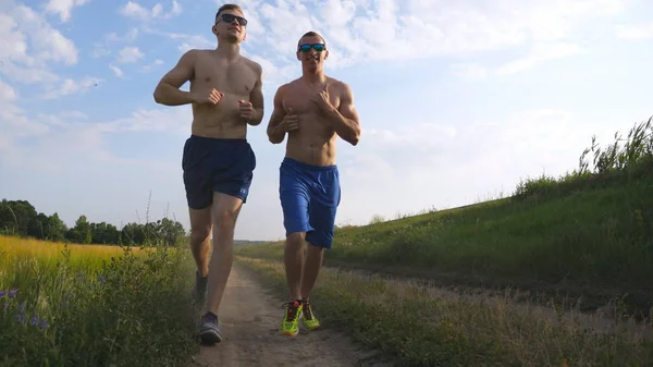 Zwei muskulöse Männer, die im Freien rennen. Junge athletische Jungs joggen über das Feld. männliche Sportler, die gemeinsam in der Natur trainieren. Freunde, die draußen trainieren. Zeitlupe gesunder, aktiver Lebensstil — Stockfoto