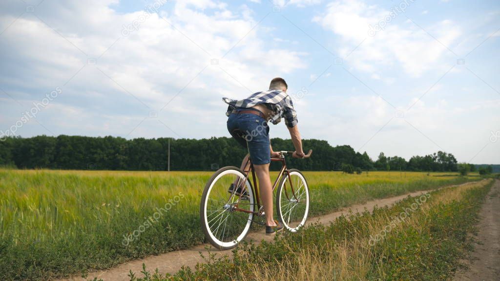 Young man riding vintage bicycle at the rural road over field. Sporty guy cycling along country trail outdoor. Male cyclist riding bike in the countryside. Healthy active lifestyle Slow motion