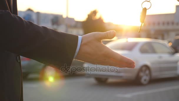 O braço do homem de negócios passa a chave do carro ao pôr-do-sol. Mãos masculinas a dar chaves de carro ao amigo. aperto de mão entre dois homens de negócios ao ar livre. Fechar câmera lenta — Vídeo de Stock