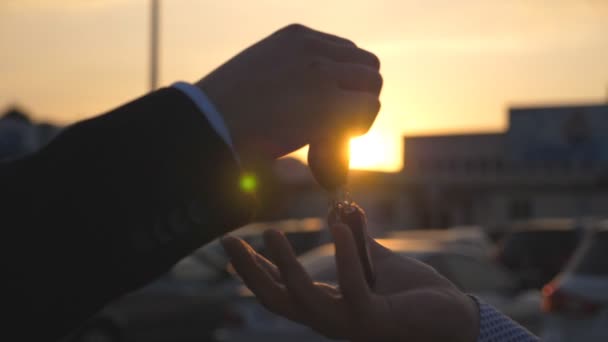 Male hands in suit giving keys of car to his friend at sunset time. Arm of businessman passes car key at evening. Handshake between two business men outdoor. Close up Slow motion — Stock Video