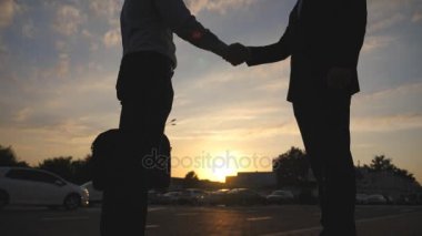 Birbirlerini tebrik kentsel ortamda günbatımında iki iş adamları. İş karşılıklı açık. Erkek silah sallayarak. İş arkadaşları karşılamak ve şehir arka planda el sıkışın. Yavaş hareket kapatmak