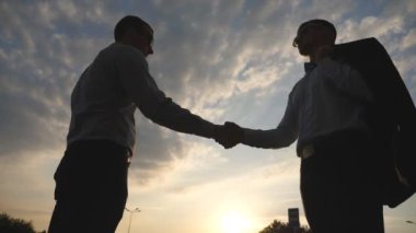 İki genç iş adamları birbirlerine arka plan, bulutlu gökyüzü ile tebrik. İş karşılıklı açık. Erkek silah sallayarak. İş arkadaşları karşılamak ve el sallamak. Yavaş hareket kapatmak