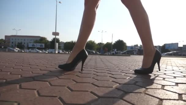 Γυναικεία πόδια στα παπούτσια ψηλά τακούνια τα πόδια στον αστικό δρόμο. Πόδια του νεαρή γυναίκα στα ψηλοτάκουνα υποδήματα πηγαίνει στην πόλη. Κορίτσι να περπατήσει για εργασία σε ηλιόλουστη μέρα. Αργή κίνηση, κοντινό πλάνο — Αρχείο Βίντεο