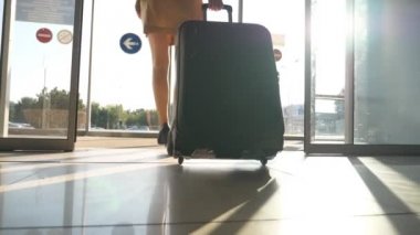 İş kadını onun Bagaj ile Havaalanı'ndan yürüme. Camdan olacak topuklu kadın sokağa kapı ve onun bavulunu tekerlekler üzerinde rulo. Güneş parlaması vasıl geçmiş. Gezi kavramı. Ağır çekim