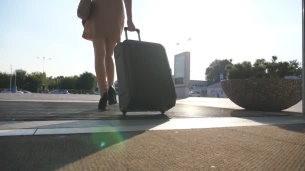 Business κυρία πρόκειται να ταξί στάθμευσης από το αεροδρόμιο με τις αποσκευές της. Κορίτσι σε τακούνια βαλίτσα να περπατήσει και ρολό πάνω σε τροχούς. Γυναίκα που περπατά με τη βαλίτσα της κατά μήκος της οδού. Έννοια του ταξιδιού. Αργή κίνηση — Αρχείο Βίντεο