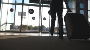 Cam otomatik kapıdan Caddesi ve rulo bavul tekerlekleri üzerinde giden adam. Onun Bagaj ile havaalanından yürüyüş iş adamı. Güneş parlaması vasıl geçmiş. Gezi veya seyahat kavramı. Ağır çekim