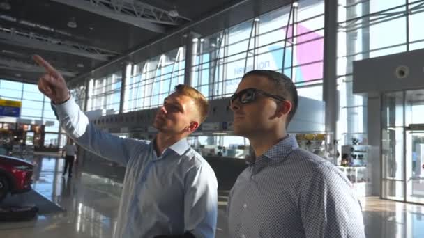 Działalności człowieka wskazując coś do jego kolega w okulary o rozkład jazdy deska ekran. Dwaj młodzi biznesmeni, patrząc na rozkład lotów na lotnisku. Kontroli linii lotniczych odlotu zwolnionym tempie z bliska — Wideo stockowe