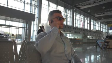 Genç ciddi iş adamı havaalanında telefonda konuşuyor. Ofiste cep telefonu konuşma güneş gözlüklü adam yakışıklı beyaz iş portresi kapatın. Ağır çekim