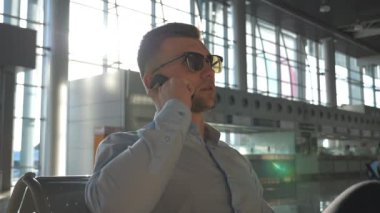 Genç mutlu işadamı vasıl geçmiş güneş parlama ile Havaalanı'nda telefonda konuşuyor. Ofiste cep telefonu konuşma güneş gözlüklü adam yakışıklı iş gülümseyen portresi kapatın. Ağır çekim