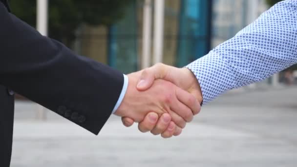 Dos hombres de negocios saludándose en un entorno urbano. Negocios apretón de manos al aire libre. Sacudiendo los brazos masculinos afuera. Colegas se encuentran y dan la mano en el fondo de la ciudad. Primer plano: cámara lenta — Vídeos de Stock