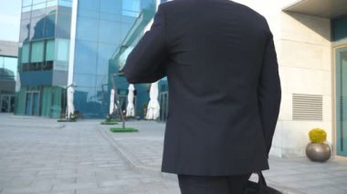 Genç işadamı için modern ofis binası yakınında yürüyüş bir çanta ile takip. Çalışmaya commuting sunglass iş adamı. Şehirde elbiseli kendine güvenen adam. Ağır çekim arka geri görüntülemek