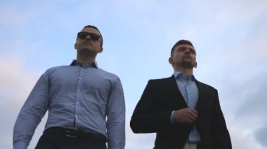 İki genç işadamları, arka plan mavi gökyüzü ile şehirde yürüyüş. Birlikte çalışmaya commuting iş erkek. Kendine güvenen çocuklar office doğru yolda olmak. İş arkadaşları açık olacak. Ağır çekim yakın çekim