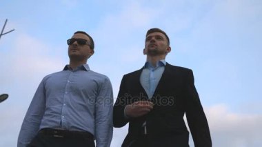 İki genç işadamları, arka plan mavi gökyüzü ile şehirde yürüyüş. Birlikte çalışmaya commuting iş erkek. Kendine güvenen çocuklar office doğru yolda olmak. İş arkadaşları açık olacak. Ağır çekim yakın çekim