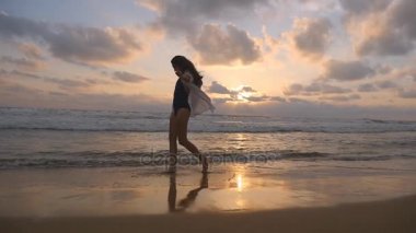 Mutlu kadın yürüyüş ve iplik sahilde okyanus yakın. Genç güzel kız hayattan zevk ve deniz sahilinde eğleniyor. Yaz tatili ya da tatil. Arka plan, günbatımı manzara. Ağır çekim