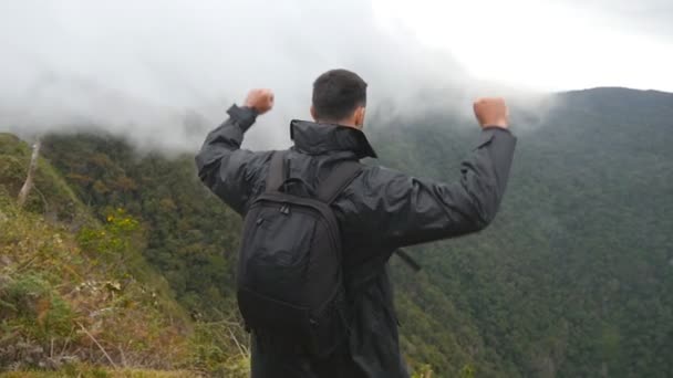 Giovane escursionista di sesso maschile con zaino che raggiunge la cima della montagna e le mani alzate. Turista uomo in piedi sul bordo del bellissimo canyon, vittoriosamente allungando le braccia. Rallentatore Retrovisore — Video Stock