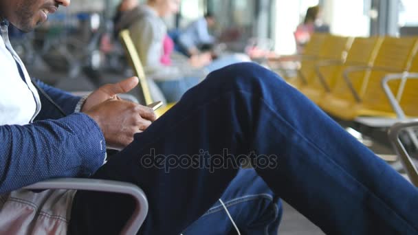 Homem indiano jovem irreconhecível usando smartphone na sala de espera do aeroporto. Mão masculina segurando celular. Um tipo a falar ao telefone. Expectativas de voo no terminal. Fechar — Vídeo de Stock