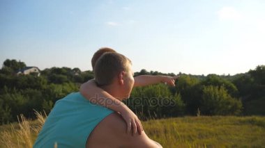 Bir şey babasına dönük ve aralarında en tepede oturan çocuk. Babası küçük oğluyla birlikte vakit açık gün batımında. Ağır çekim arka geri görüntülemek