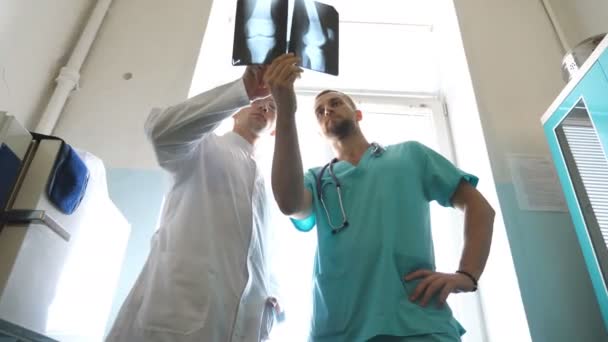 Два кавказских врача смотрят на МРТ и обсуждают это. Медработники в больнице проверяют рентгеновские снимки. Мужчины-медики консультируются друг с другом при взгляде на рентгеновское изображение. Закрыть — стоковое видео