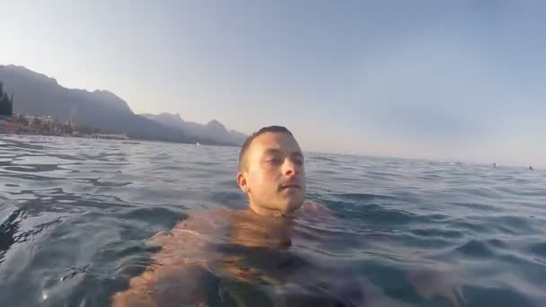 Молодий чоловік посилає привітання з моря під час літніх канікул. Усміхнений хлопець плаває і робить автопортрет. Концепція свята. Повільний рух — стокове відео