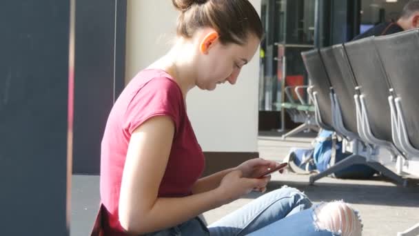 Mujer joven usando smartphone en la sala de espera del aeropuerto. Chica con teléfono inteligente en la terminal durante las expectativas de vuelo. De cerca. — Vídeo de stock