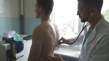 Doktor kontrol sırt ve göğüs Hastanesi ofisinde bir adam. Doktor muayene genç erkek hasta stetoskop ile. Tıbbi işçi dinleme kalp atışı atletik adam. Yakın çekim