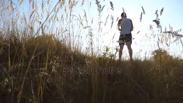 Un chico deportivo caminando por el campo. Un joven va al campo de verano. Deporte y estilo de vida activo. Movimiento lento Ángulo de visión baja — Vídeos de Stock