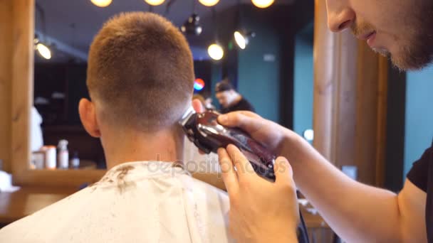 Парикмахер стрижет волосы клиента-мужчины клиппером в парикмахерской. Процесс прически. Медленное движение — стоковое видео