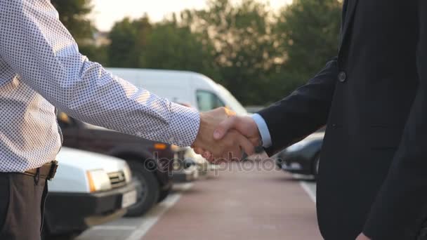 Två affärsmän skakar hand med varandra med bilar i parkering på bakgrunden. Handslag mellan chef eller återförsäljare och kund. Skakningar av manliga armar utanför. Närbild Slow motion — Stockvideo
