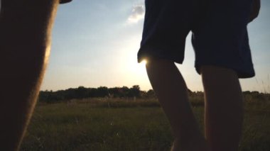 Baba ve oğul sahada günbatımında yürüyüş ve birbirlerinin ellerini tutarak. Mutlu aile birlikte vakit açık. Aktif yaşam tarzı. Ağır çekim arka geri görüntülemek