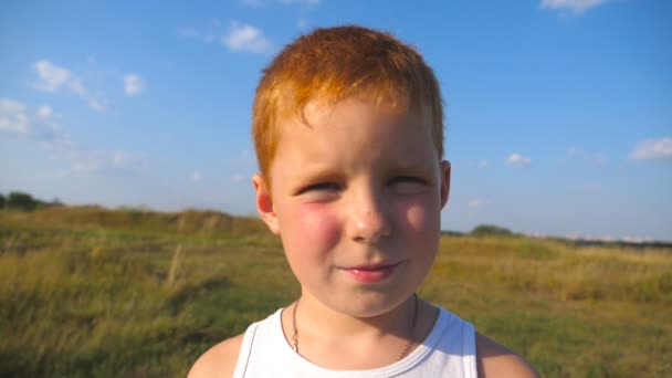 屋外の笑みを浮かべてそばかすが若い赤毛の少年の肖像画。うれしそうな笑顔でカメラに探している愛らしい子です。幸せな子供時代のコンセプトです。スローモーションを閉じる — ストック動画