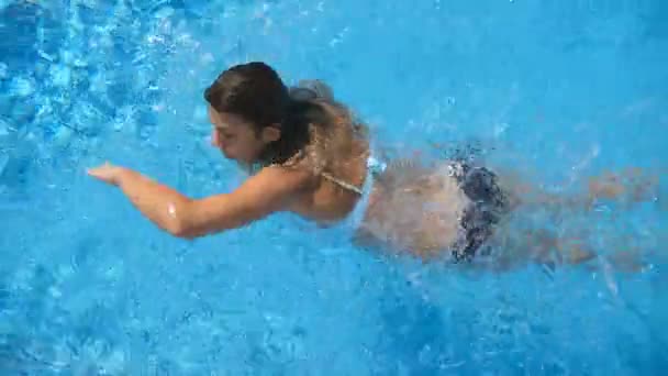 Joven hermosa chica nadando en la piscina. Morena relajante en agua tibia clara en un día soleado. Vista superior Cerrar Cámara lenta — Vídeo de stock