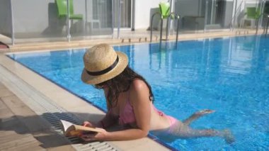 Şapka ve güneş gözlüğü havuz kitap okuma güzel kız. Genç kadın rahatlatıcı tatil sırasında sıcak güneşli gün. Yaz tatil kavramı. Yan görünümü kapatmak yavaş hareket