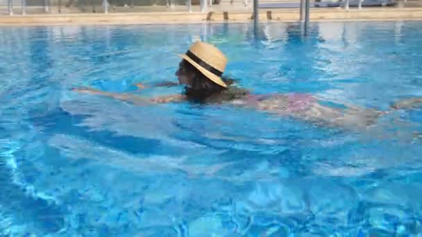 Fiatal gyönyörű lány napszemüveg és kalap úszás medencében. Nő, kellemes, tiszta meleg vízben napsütéses napon. Nyári nyaralás vagy hétvégi koncepció. Lassú mozgás közelről — Stock videók