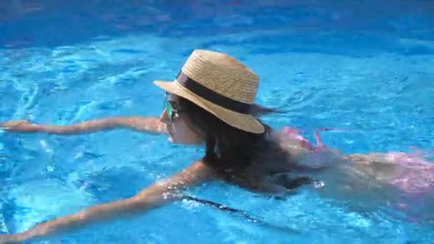 Young beautiful girl in sunglasses and hat swimming in pool. Woman relaxing in clear warm water on sunny day. Summer vacation or holiday concept. Close up Slow motion — Stock Video