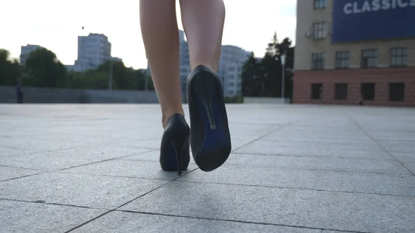Folgen Sie weiblichen Beinen in Stöckelschuhen, die durch die urbane Straße gehen. Füße einer jungen Geschäftsfrau in hochhackigen Schuhen, die in der Stadt unterwegs ist. Mädchen auf dem Weg zur Arbeit. Zeitlupe Nahaufnahme Rückseite — Stockfoto
