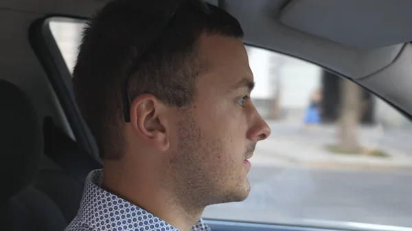 Νεαρός επιχειρηματίας στο πουκάμισο οδήγηση αυτοκινήτου στην πόλη και την ομιλία. Καυκάσιος άνθρωπος με σοβαρό πρόσωπο οδήγηση auto και μιλάμε. Πλαϊνή θέα από το σαλόνι. Αργή κίνηση — Φωτογραφία Αρχείου