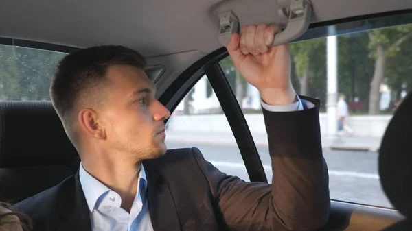 Young businessman sitting on the backseat in the car and talking. Man sits on a seat at the back of auto and speaking. Guy while traveling inside of taxi saying something to driver. Close up Slow mo