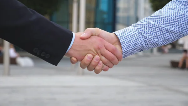 Des collègues se rencontrent et se serrent la main dans l'arrière-plan de la ville. Deux hommes d'affaires se saluent en milieu urbain. Poignée de main en plein air. Secouement des bras masculins dehors. Gros plan Mouvement lent — Photo