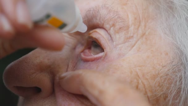 Ηλικιωμένη γυναίκα που στάζει ιατρική σταγόνες στο μάτι της. Προσωπογραφία της γιαγιάς. Υγειονομική περίθαλψη και ιατρική αντίληψη. Εσωτερικη αργή κίνηση — Αρχείο Βίντεο