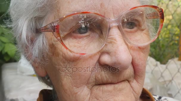 Eine alte Frau mit Brille blickt nach vorn und lächelt. Porträt einer glücklichen Oma mit Brille, die Zeit im Freien verbringt. Gefühle der Großmutter. Nahaufnahme Zeitlupe