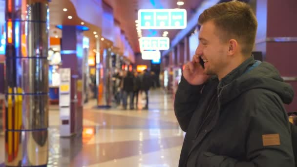 Un joven guapo hablando por celular en el centro comercial. Feliz chico sonriente hablando en el interior del teléfono inteligente. De cerca. — Vídeos de Stock