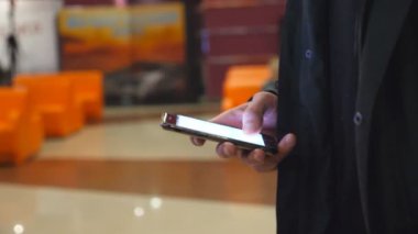 Alışveriş merkezinde yürüyüş ve smartphone kullanarak adam. Gözatma bilgilerinin ve akıllı telefon resimleri kaydırma erkek eller. Yakın çekim