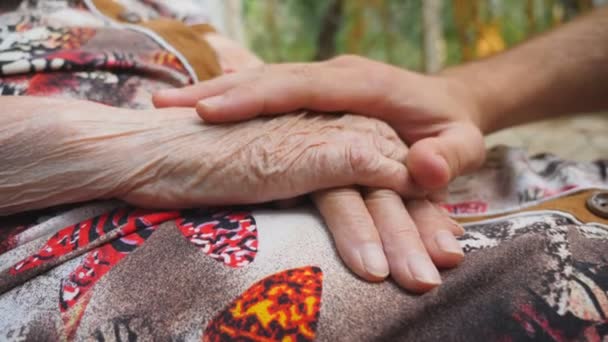 Joven manos masculinas consolando a un anciano brazos de la abuela al aire libre. El nieto y la abuela pasan tiempo juntos afuera. Concepto de cuidado y amor. Vista lateral Vista lenta — Vídeos de Stock