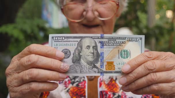 戴眼镜的老妇人把比尔的100美元放在相机里, 面带微笑。奶奶在外面拿现金金钱概念。关闭慢动作 — 图库视频影像