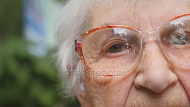 Dolly tiro de anciana en gafas al aire libre. Ojos de una anciana con arrugas a su alrededor. Primer retrato de la abuela afuera. Movimiento lento — Vídeo de stock