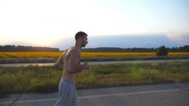 Ülkede yol günbatımında koşu kas delikanlı. Erkek koşucu için maratona profil açık çalıştırın. Mavi gökyüzü güneş ile karşı egzersiz atlet. Spor ve aktif yaşam tarzı. Ağır çekim