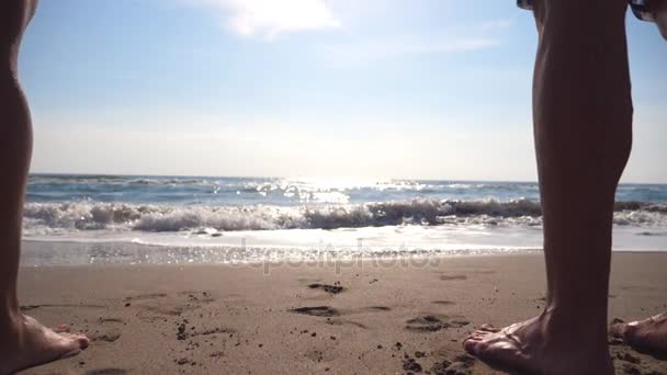 Joven hombre y mujer de pie en la orilla y disfrutando del mar al amanecer. Olas tranquilas del océano rodando en la playa de arena. Vacaciones de verano o vacaciones. Primer plano Ángulo de visión bajo Movimiento lento — Vídeo de stock