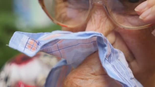 Großmutter mit Brille, die ihre Nase ins Taschentuch pustet. Porträt einer kranken alten Frau. Zeitlupe in Nahaufnahme