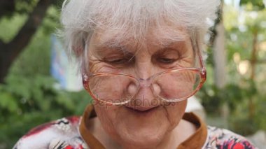 Yaşlı kadında bir şey okuma ve açık gülümseyen gözlük. Gözlük dışında vakit mutlu granny portresi. Duygular büyükanne. Yavaş hareket kapatmak